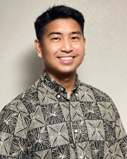 The image shows a person smiling at the camera. They are wearing a patterned shirt with a floral design and have short hair.
