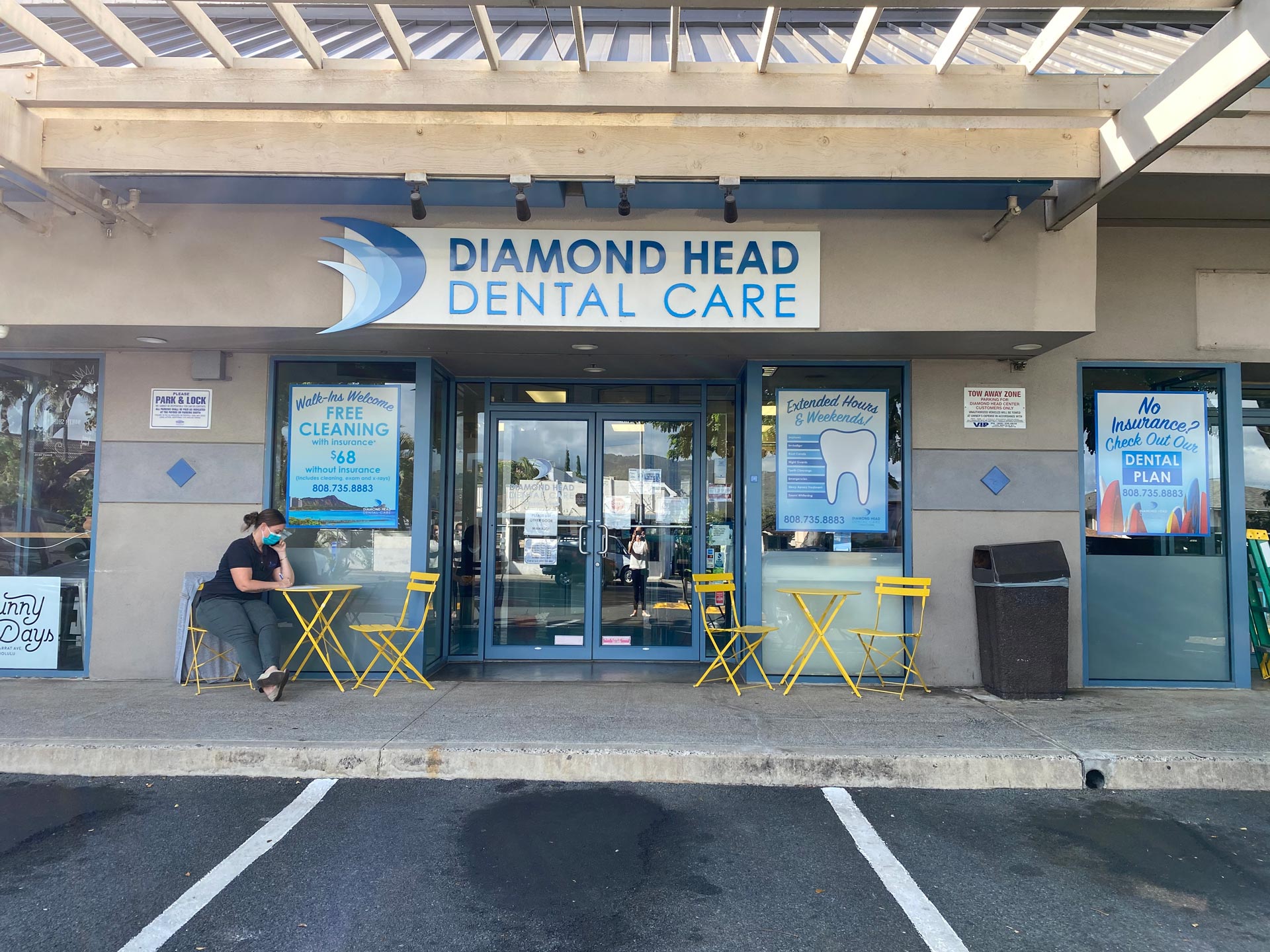 The image shows a storefront with a sign reading  Diamond Head Dental Care  and a person sitting at an outdoor table.
