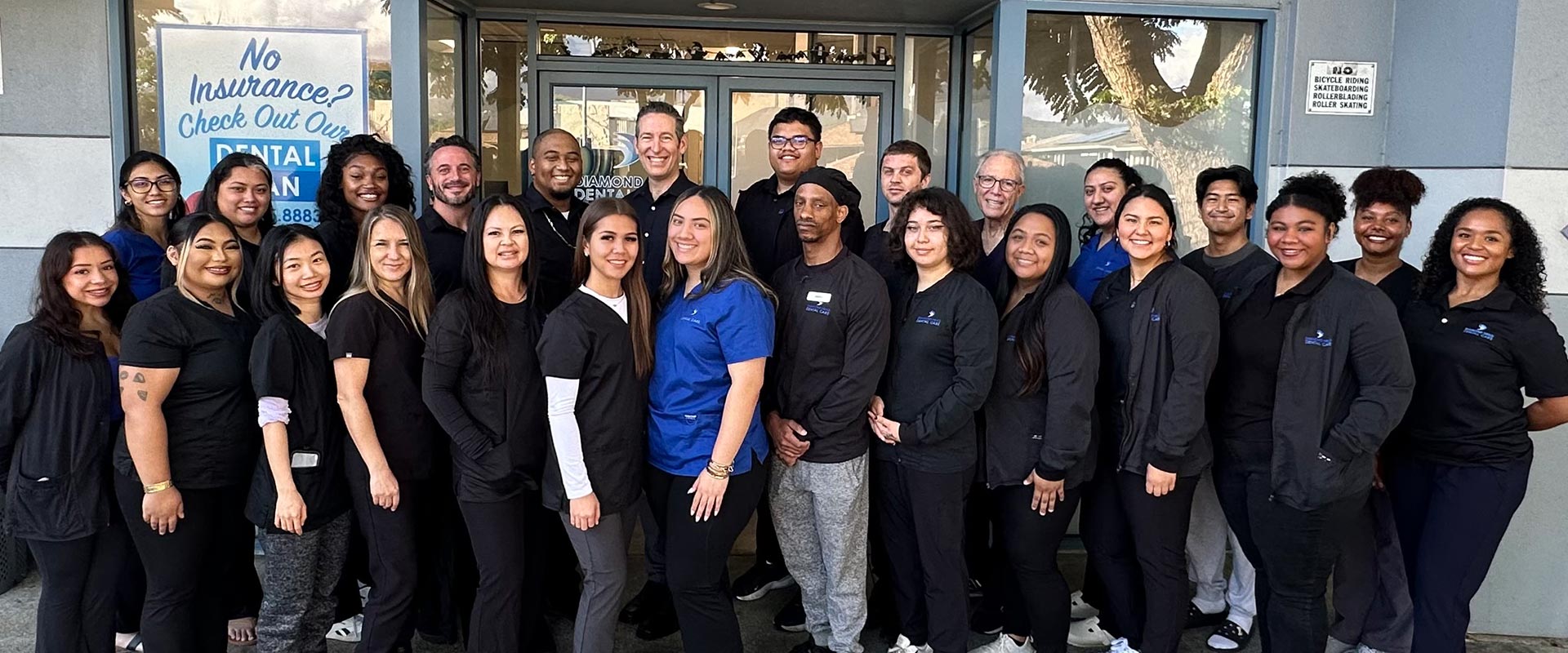 This is a photograph of a group of people posing together outside a building with a sign that reads  NO ENTRANCE.