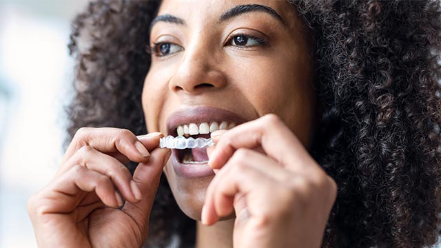 The image features a smiling woman with curly hair holding a toothbrush with toothpaste, looking directly at the camera.