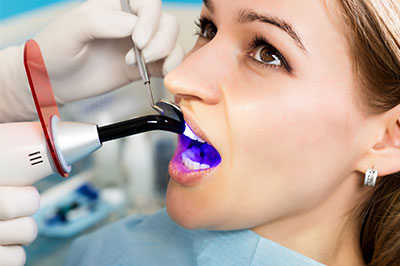 A woman receiving dental treatment with a device inserted into her mouth by a professional in a medical setting.