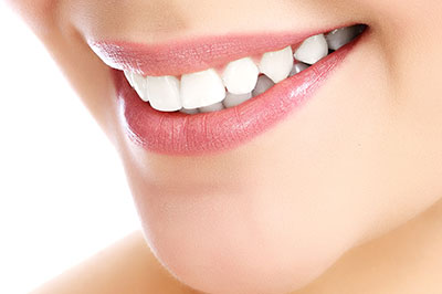 The image shows a close-up view of a person smiling with their teeth visible, featuring fair skin and pink lips.