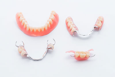 The image shows a collection of dentures with red gums and sharp teeth displayed on a white surface.