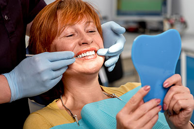 The image shows a woman sitting in a dental chair with a blue mouthpiece on her teeth, being attended to by a dental professional who appears to be adjusting her smile.