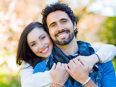 A man and woman hugging each other closely outdoors, smiling broadly.