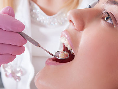 A woman receiving dental treatment with a dentist using a drill on her teeth.