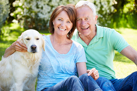 The image features an older couple sitting outdoors with a golden retriever dog between them, smiling and enjoying each other s company.