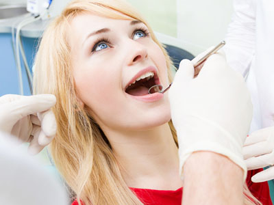 The image shows a woman sitting in a dental chair with her mouth open, receiving dental treatment from a dentist who appears to be performing a procedure on her teeth.
