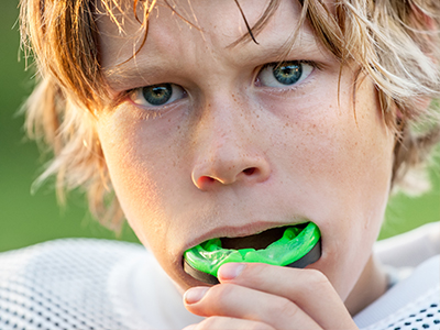 The image shows two photographs of a young boy with blonde hair, wearing a football jersey, holding a toothbrush in his mouth, with one photo capturing him looking directly at the camera while the other has him looking away.