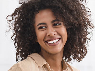 A woman with curly hair and a bright smile, wearing a beige top, poses for the camera.